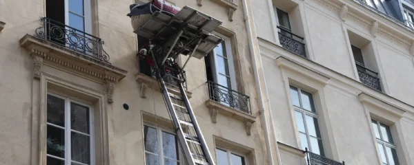 Deux déménageurs descendent un canapé emballé à l'aide d'un monte-meuble installé devant une maison à colombages dans le Tarn-et-Garonne.