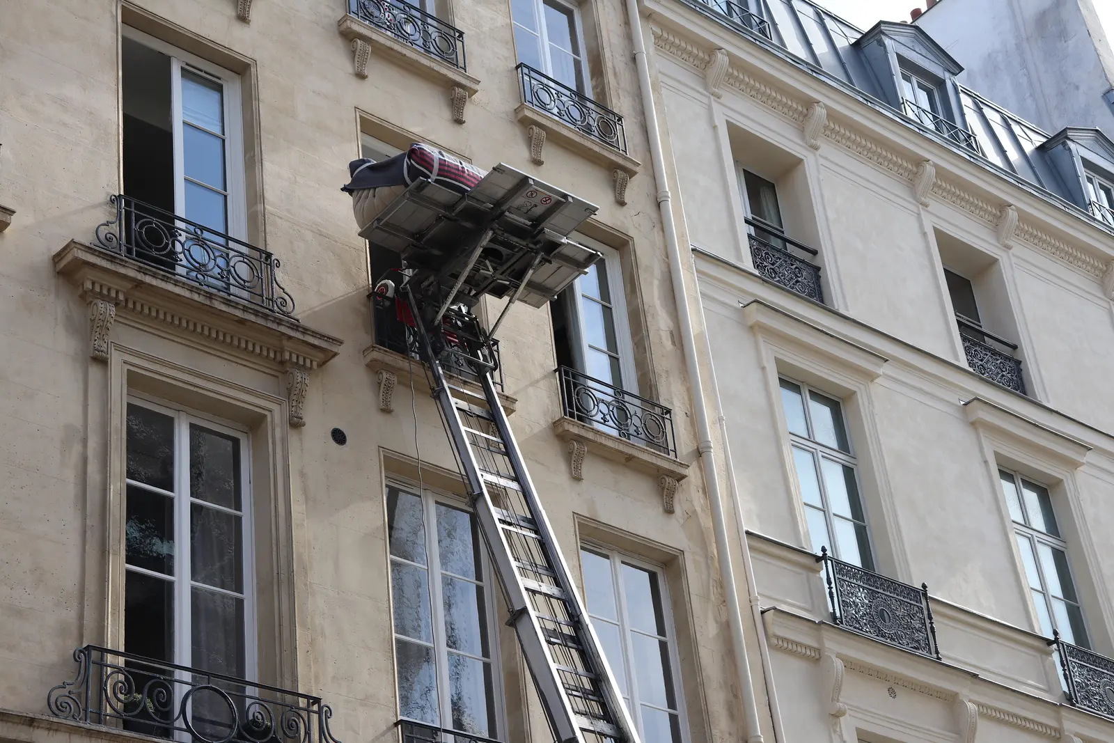 Deux déménageurs descendent un canapé emballé à l'aide d'un monte-meuble installé devant une maison à colombages dans le Tarn-et-Garonne.